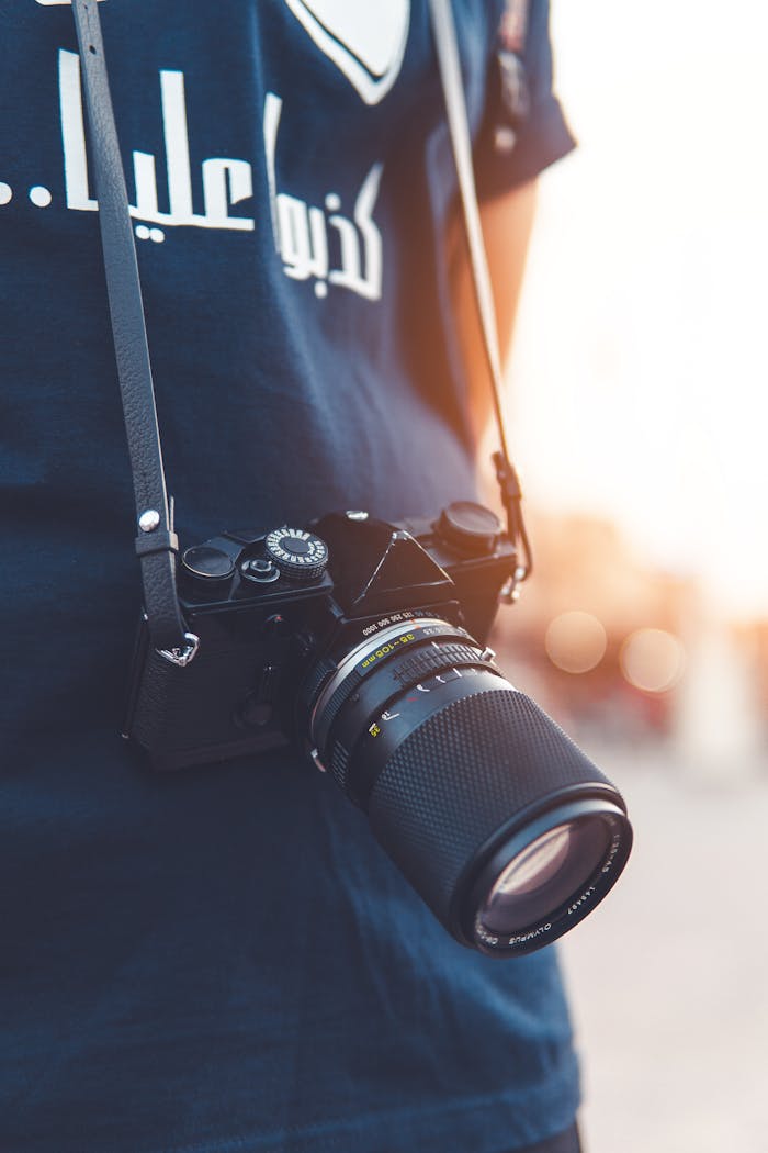 Close-up view of a vintage camera hanging from a strap on a person, capturing the essence of street photography.